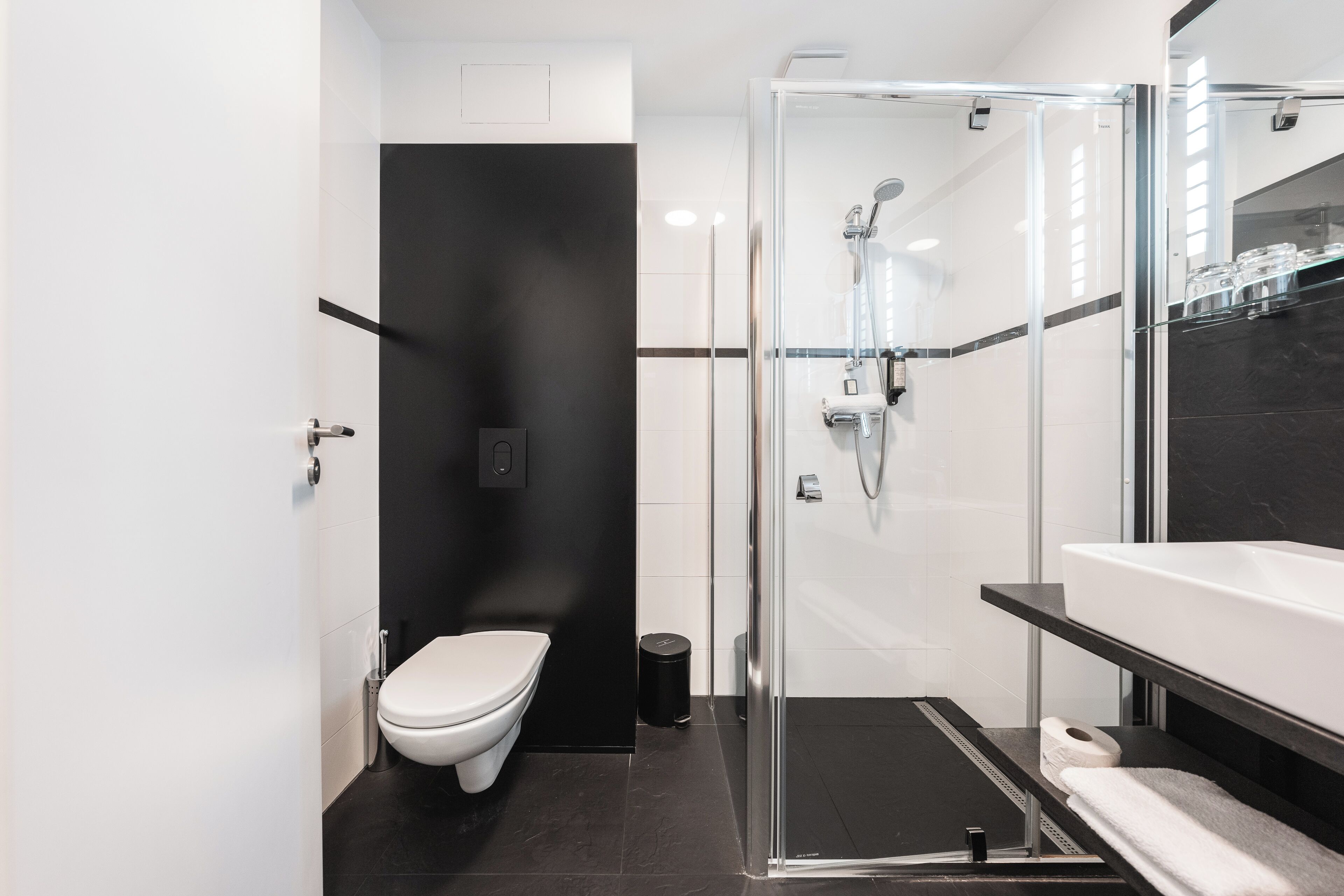 A modern bathroom with a glass-enclosed shower, a white toilet, and a black-tiled floor.