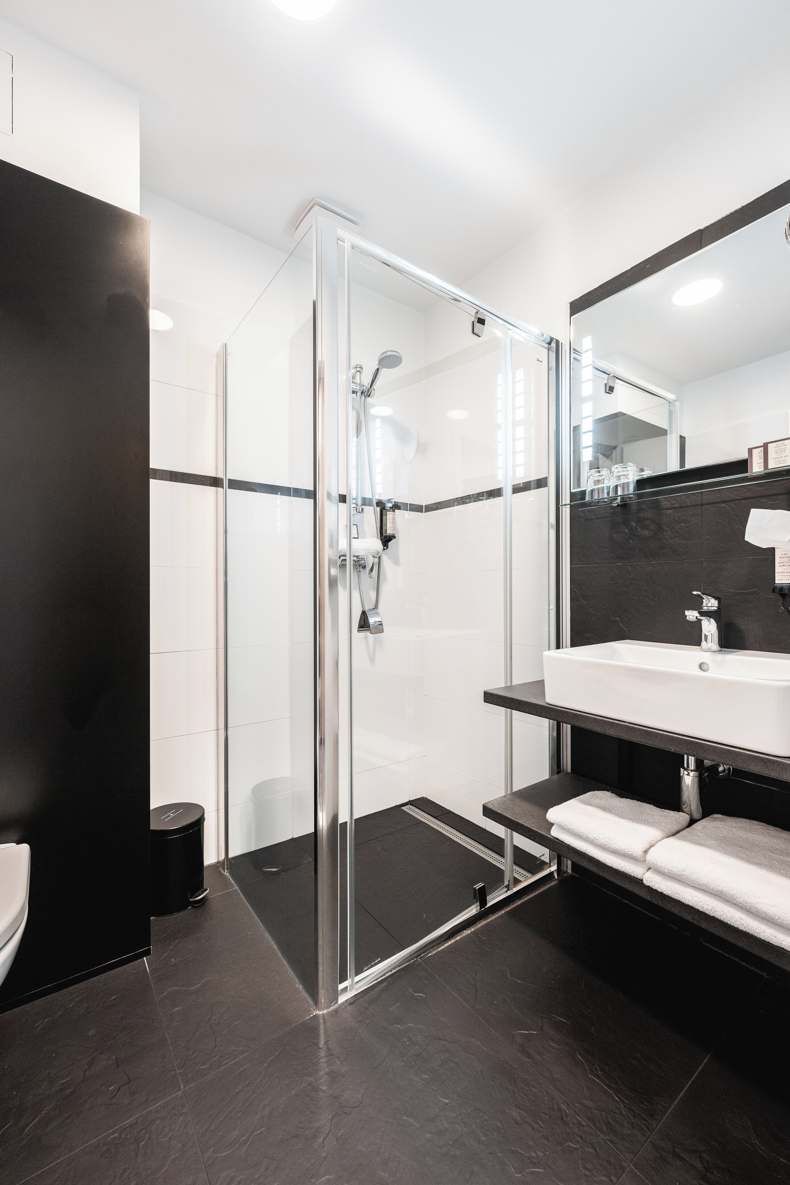 Une salle de bain moderne avec une douche à parois de verre, un lavabo blanc et un sol foncé.