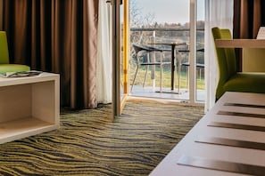 A hotel room with a large window, a green chair, a white table, and a patterned carpet. - Maximus Resort (Brno)