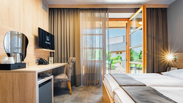 A hotel room with a bed, a desk with a telephone, a television, and a view of the outdoors. - Maximus Resort (Brno)