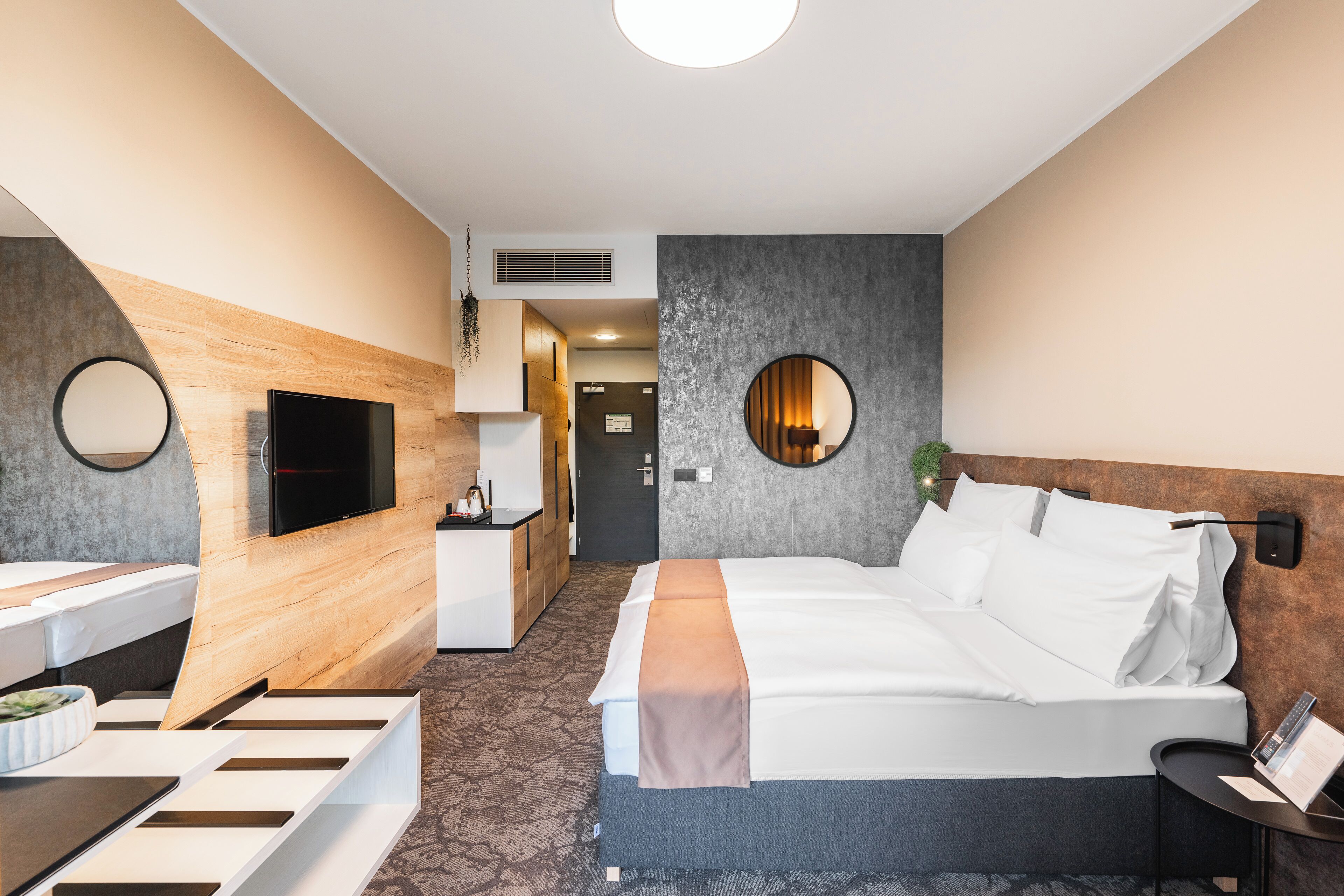 Una habitación de hotel moderna con una cama, un escritorio, un televisor y un espejo circular en la pared.