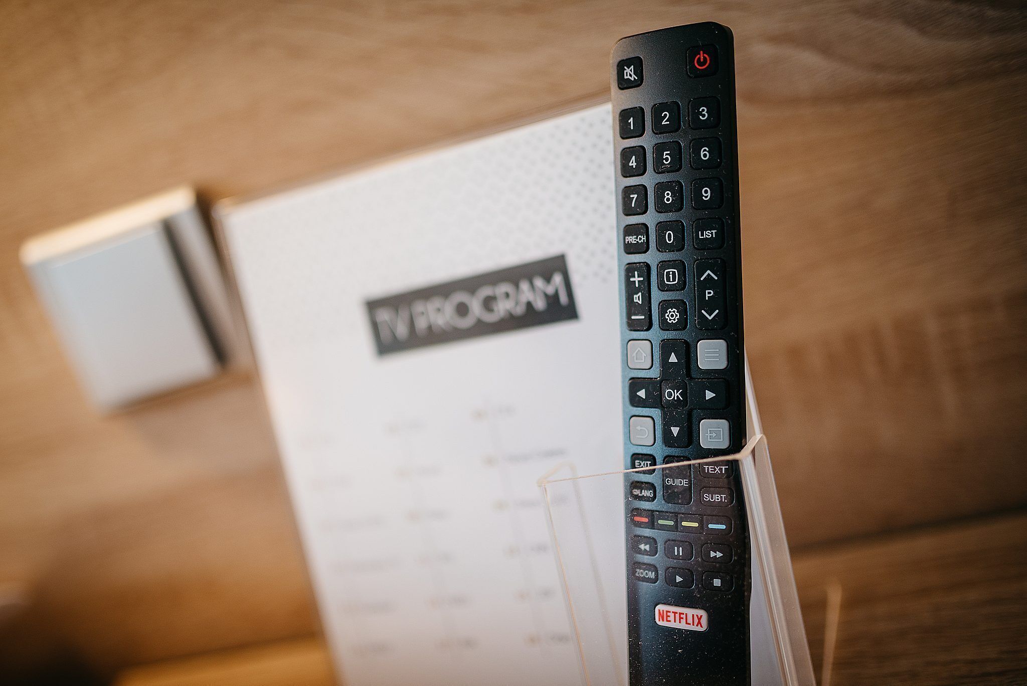 A black remote control with a Netflix logo, placed on a wooden surface with a menu card in the background.