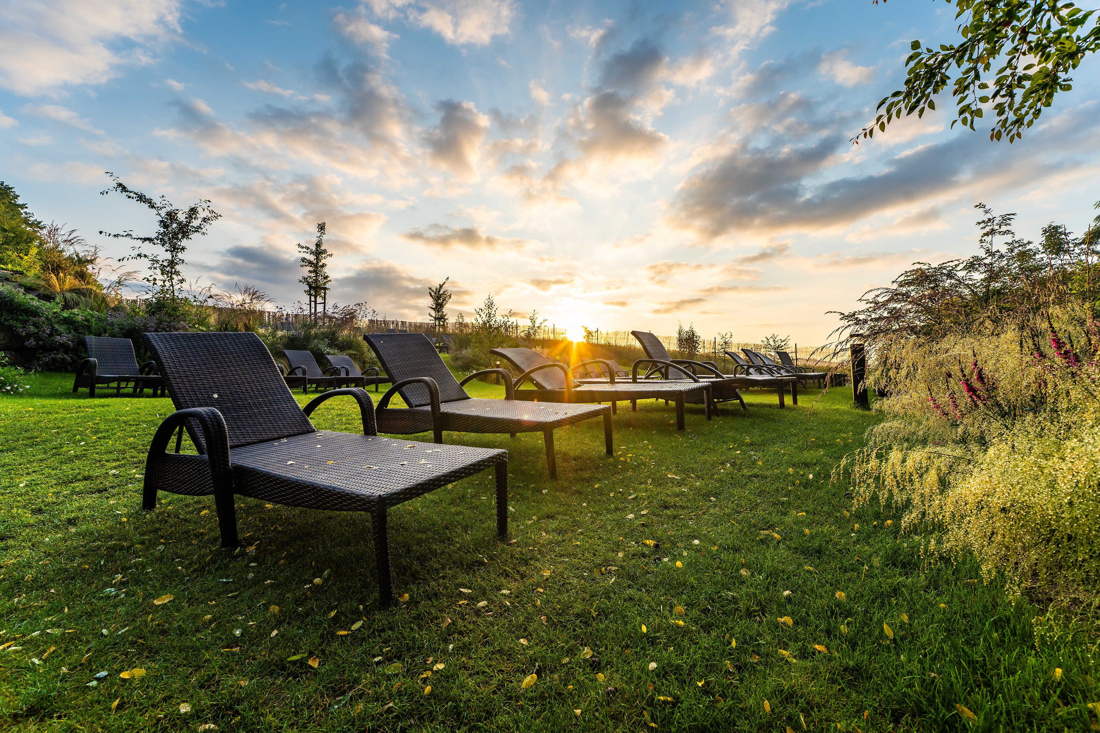 Des fauteuils de jardin sont disposés sur une pelouse verdoyante, avec un coucher de soleil en arrière-plan.
