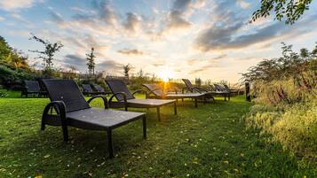 Des fauteuils de jardin sont disposés sur une pelouse verdoyante, avec un coucher de soleil en arrière-plan.