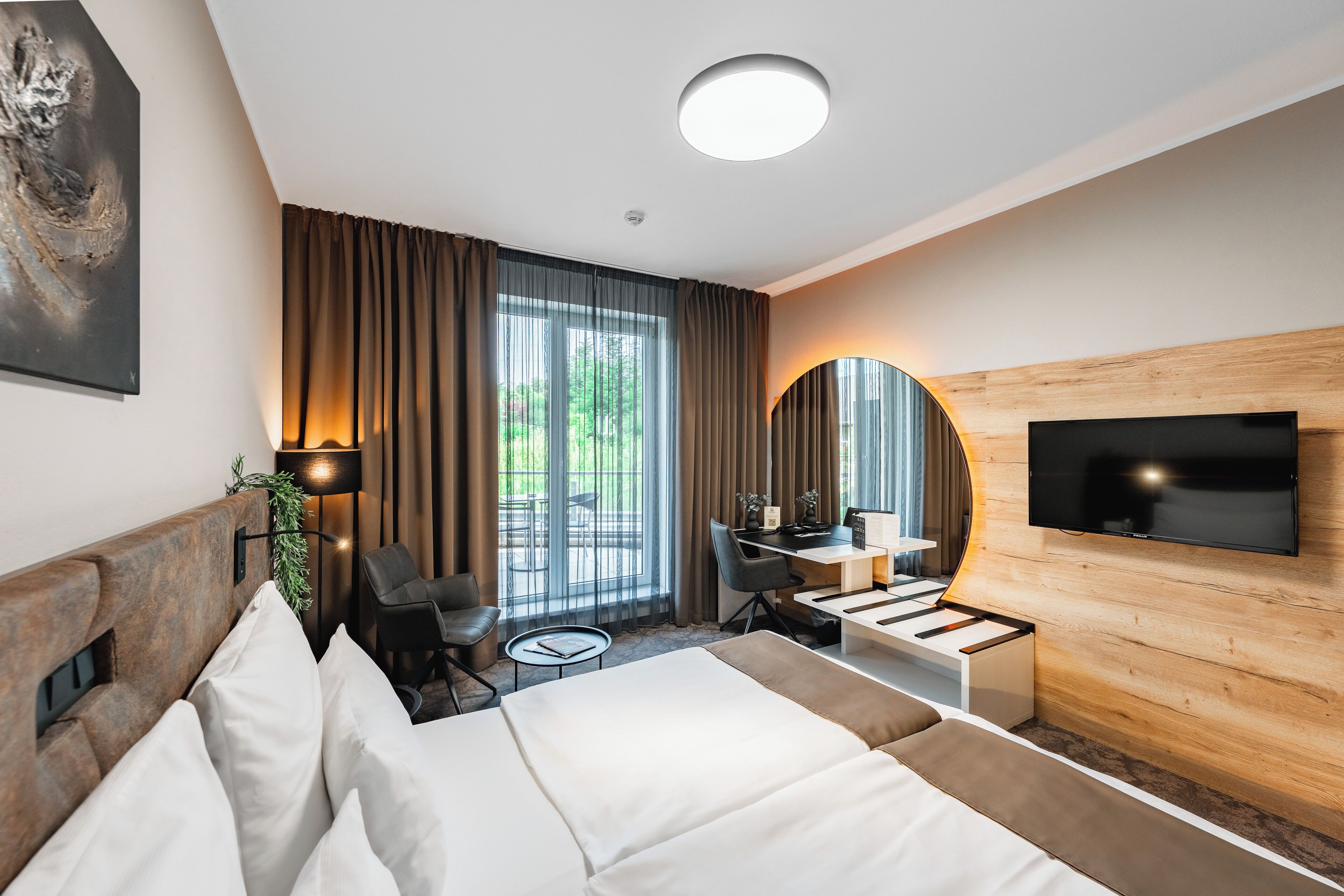 Ein modernes Hotelzimmer mit Bett, Schreibtisch, Stuhl, Fernseher und großen Fenstern.