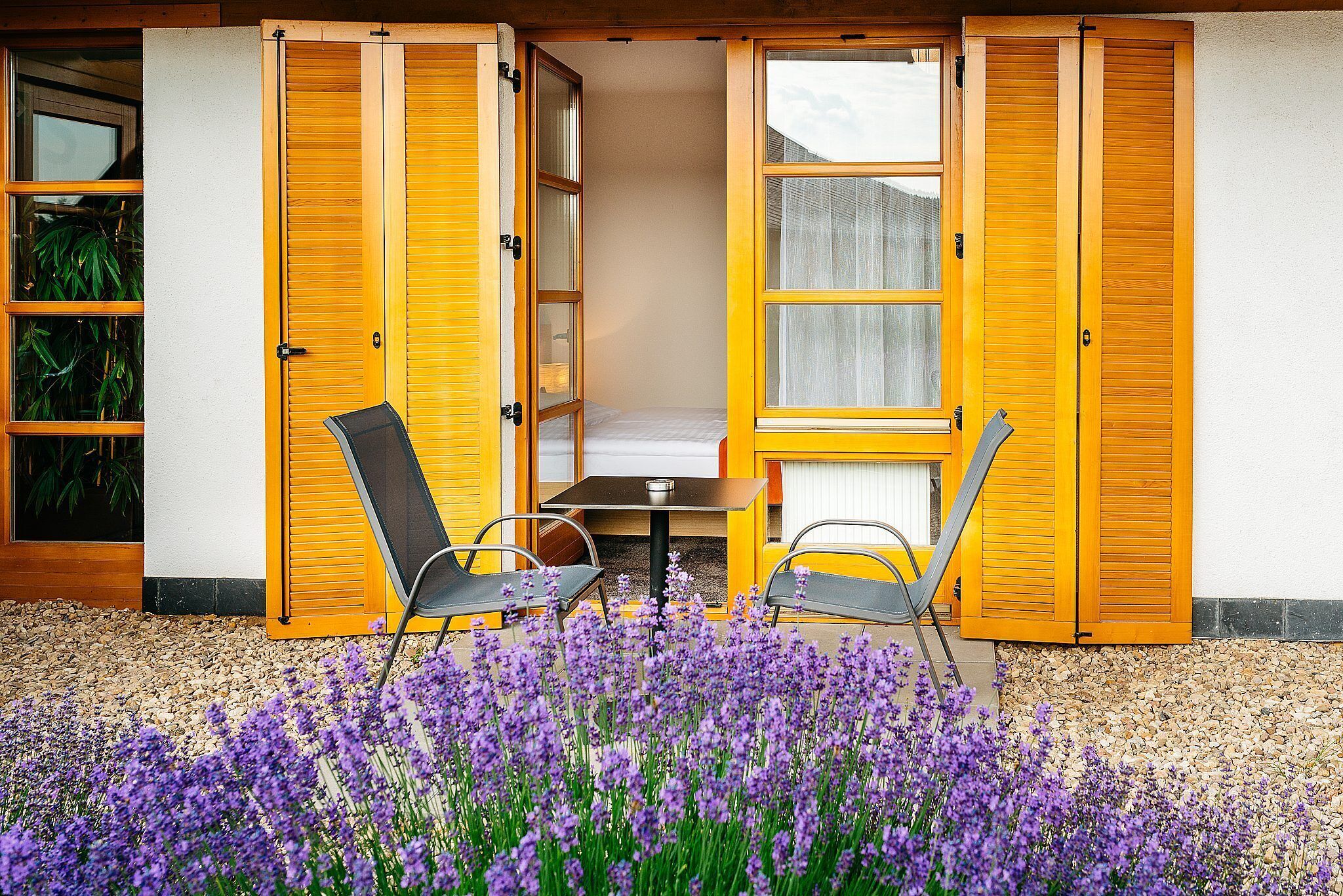 A room with a bed, a table, and two chairs. There is a window with blinds and a door with a handle.