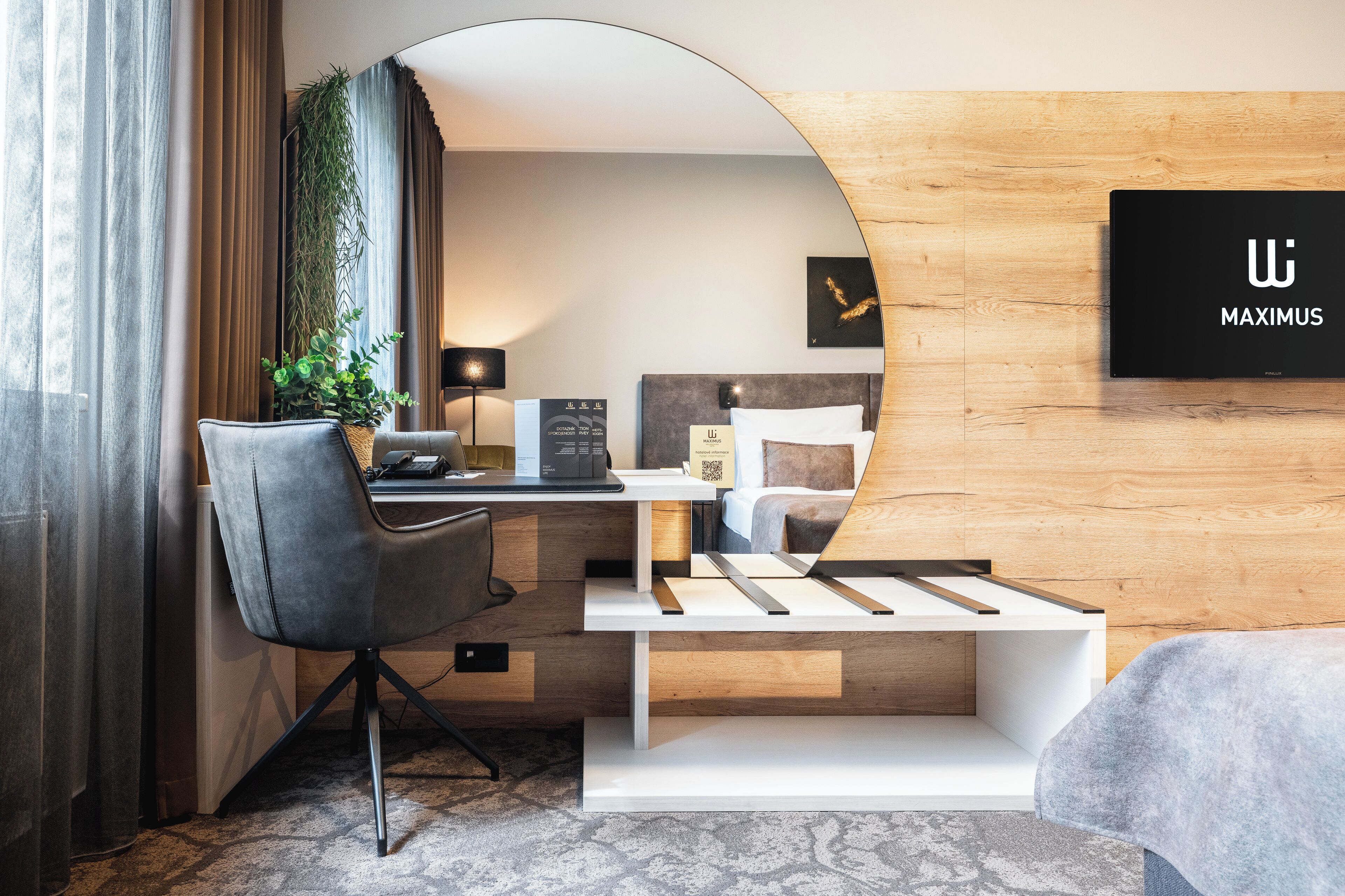 A modern hotel room with a desk, chair, bed, and a large mirror.