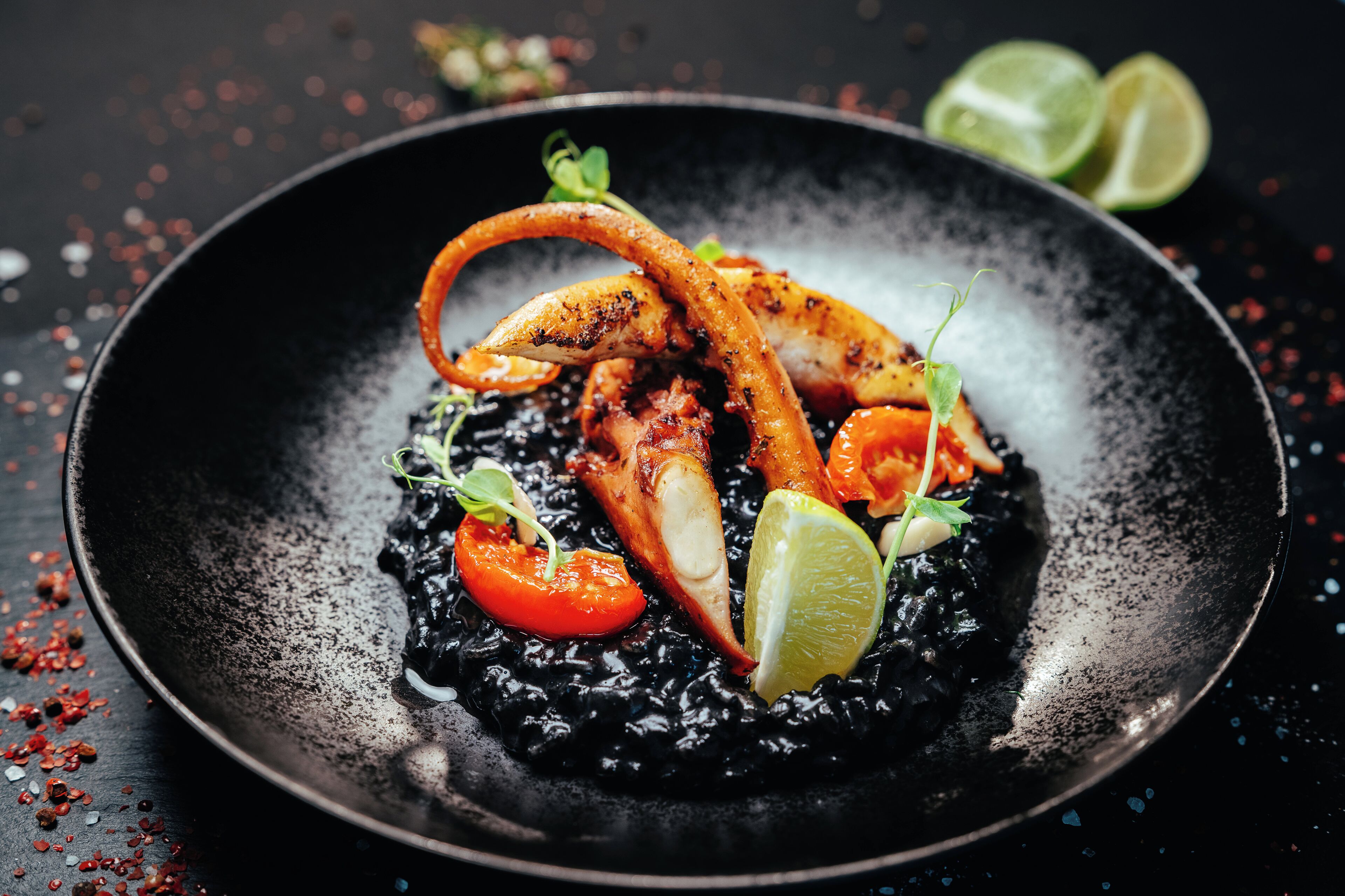 Un plato negro con un plato de mariscos, decorado con hierbas y lima.