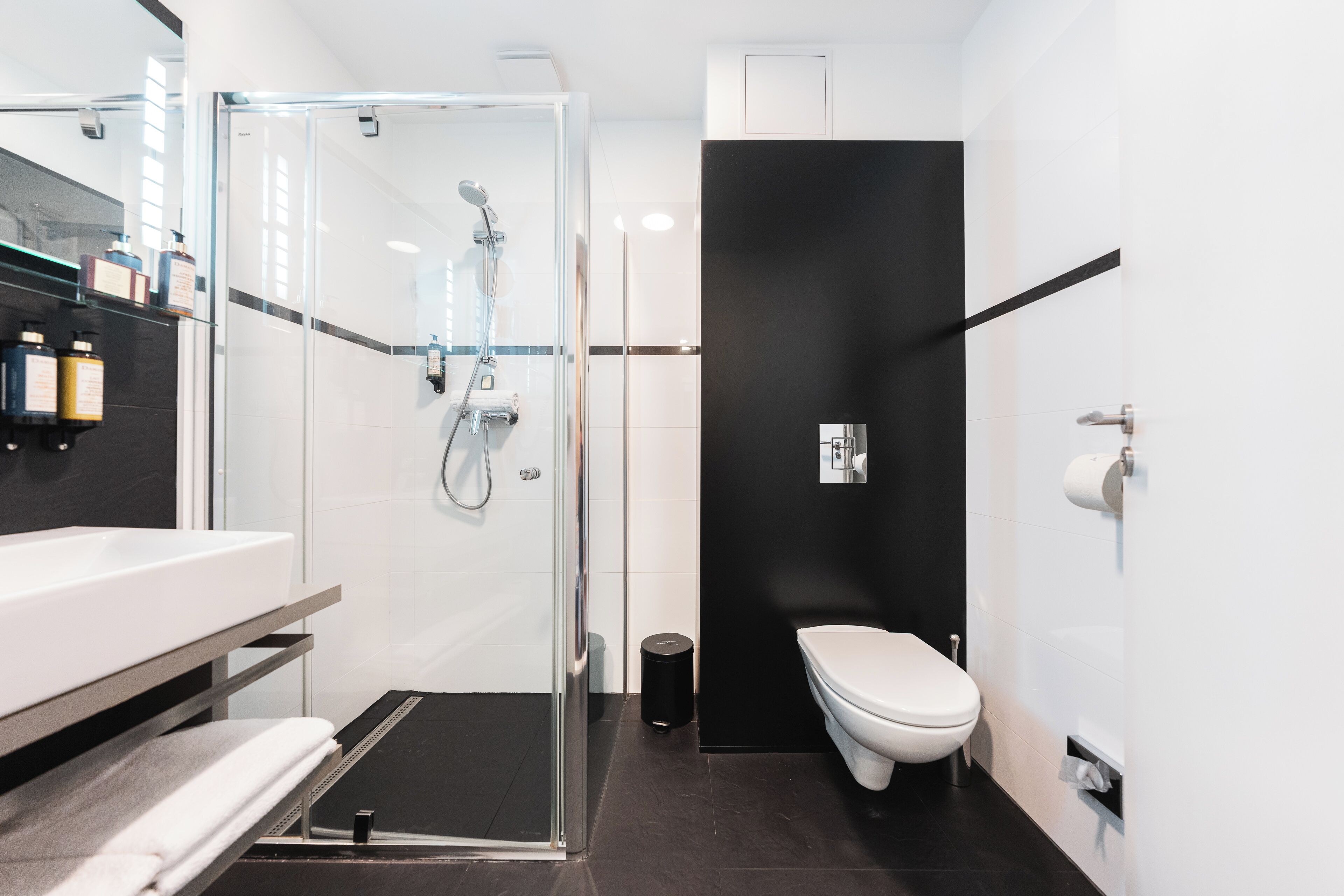A modern bathroom with a glass shower enclosure, a white toilet, and a sink with a towel rack.