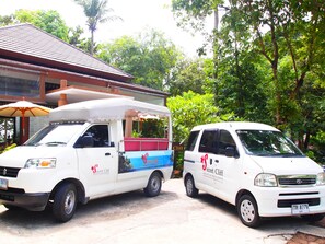 Two white vans parked in front of a building with a red roof, one with a blue and red awning. - Secret Cliff Villa (Karon)