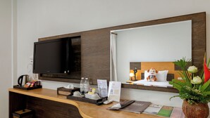 A hotel reception desk with a flat-screen TV, a wooden counter, a mirror, a plush toy, a vase with flowers, and various amenities like a kettle, coffee maker, and informational brochures. - Secret Cliff Villa (Karon)