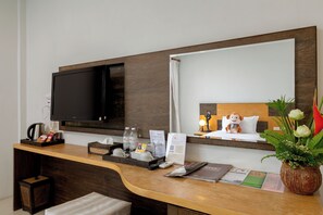 A hotel room with a TV, a wooden desk, a mirror, a bed, and a plant. - Secret Cliff Villa (Karon)