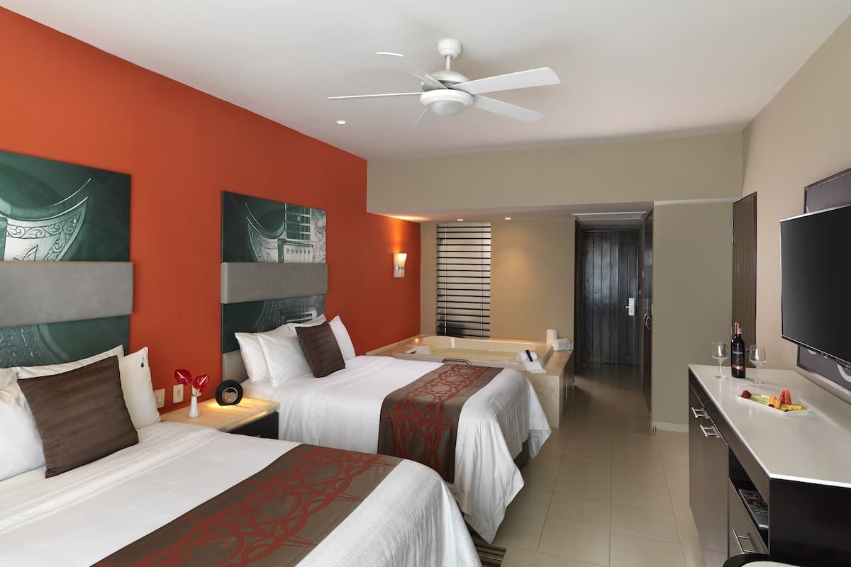 Una habitación de hotel con dos camas, televisión, escritorio y baño con bañera.