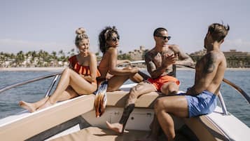 Un groupe de personnes se trouve sur un bateau, d’où l’on a une vue dégagée sur une plage et des palmiers en arrière-plan.
