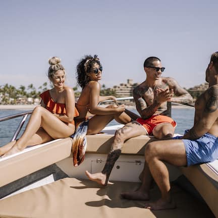 A group of people on a boat with a clear view of a beach and palm trees in the background.