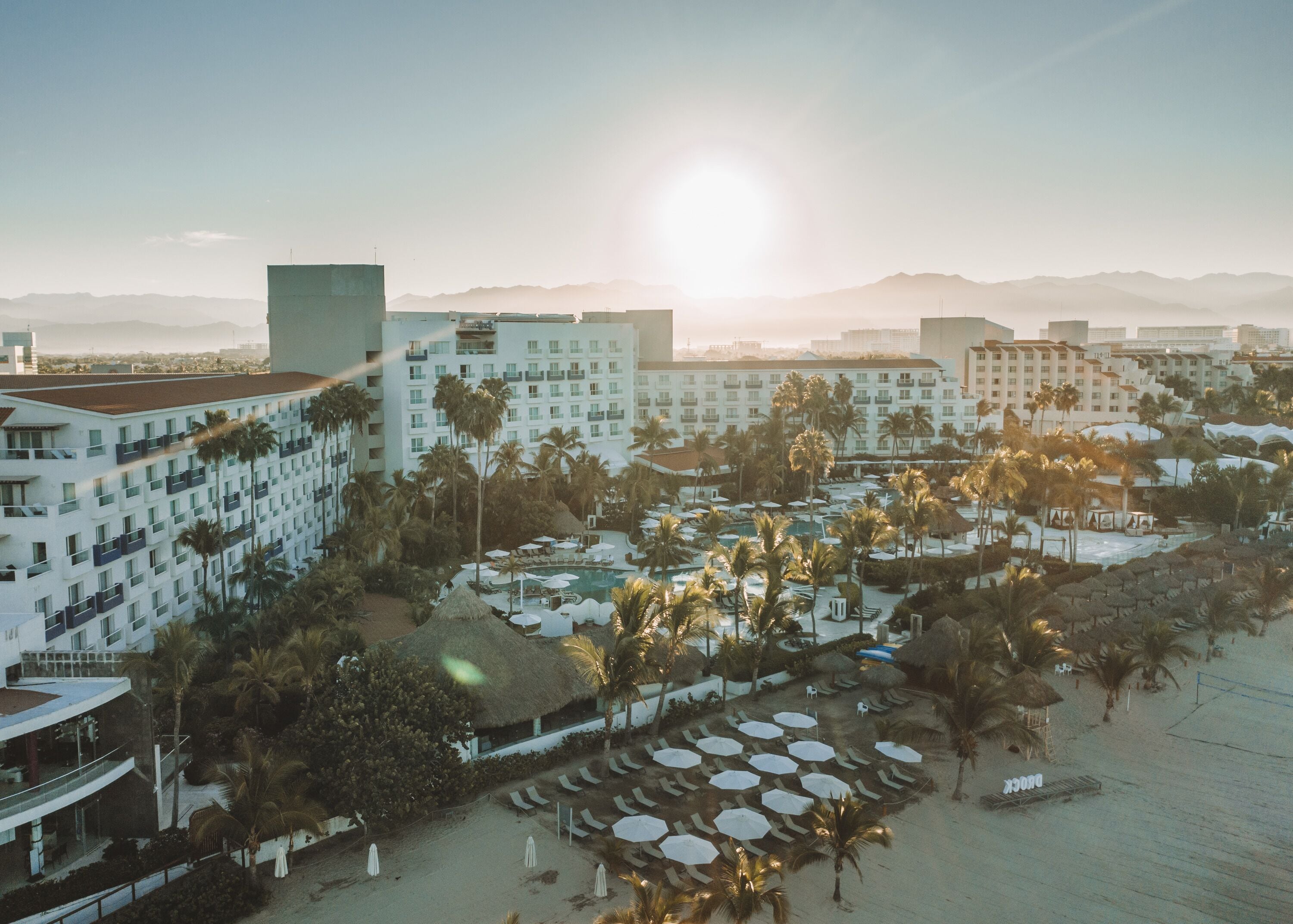 Un resort con varias edificaciones, un área de piscina y una playa con tumbonas.