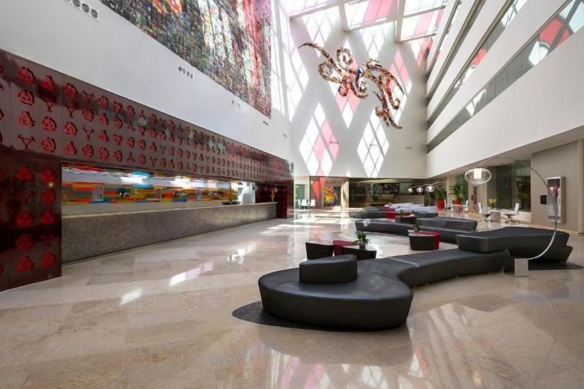 A spacious lobby with a modern design, featuring a reception desk, seating areas, and a large window allowing natural light.