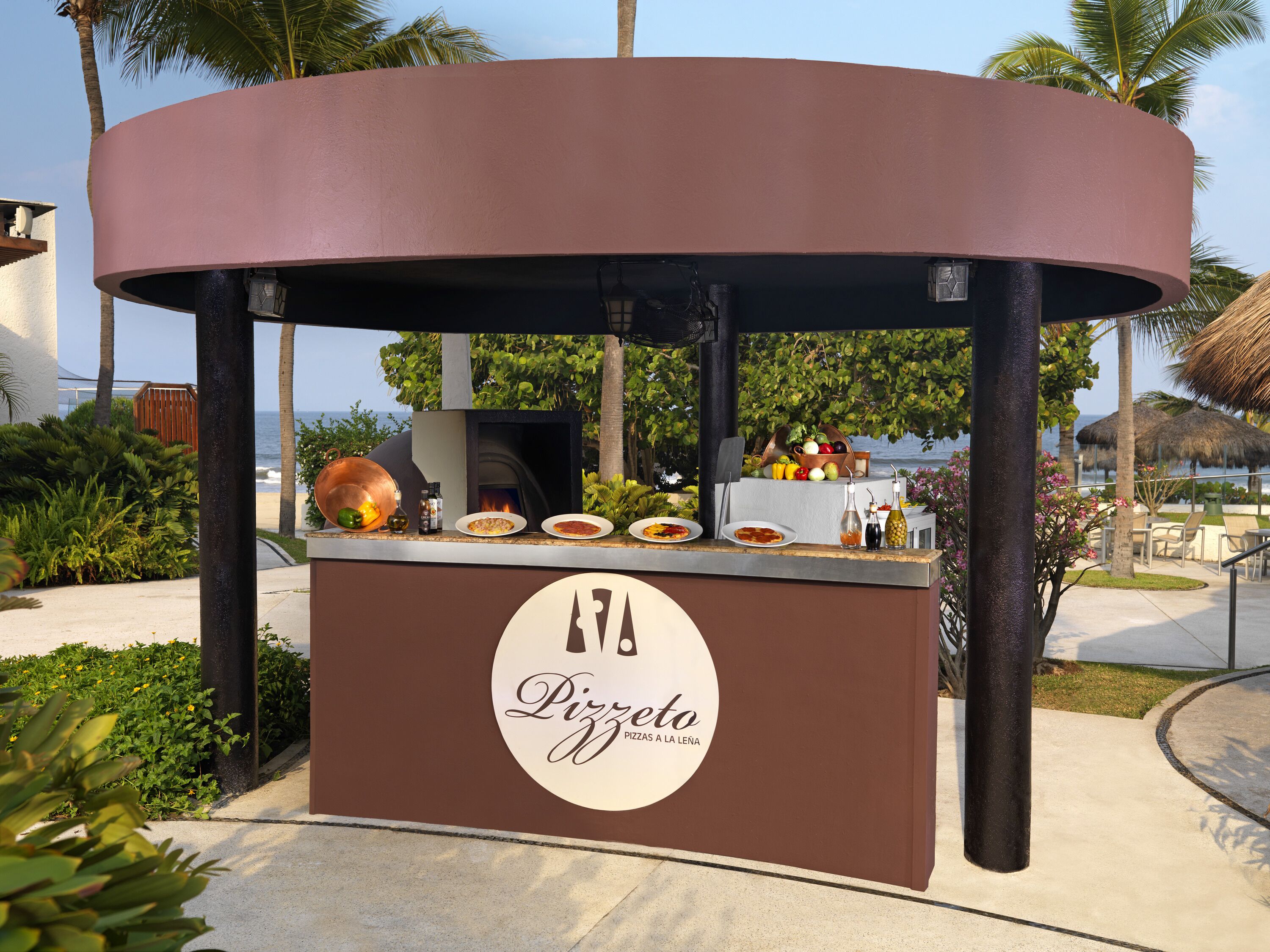 An outdoor pizza kiosk with a branded logo, a pizza oven, and various condiments.