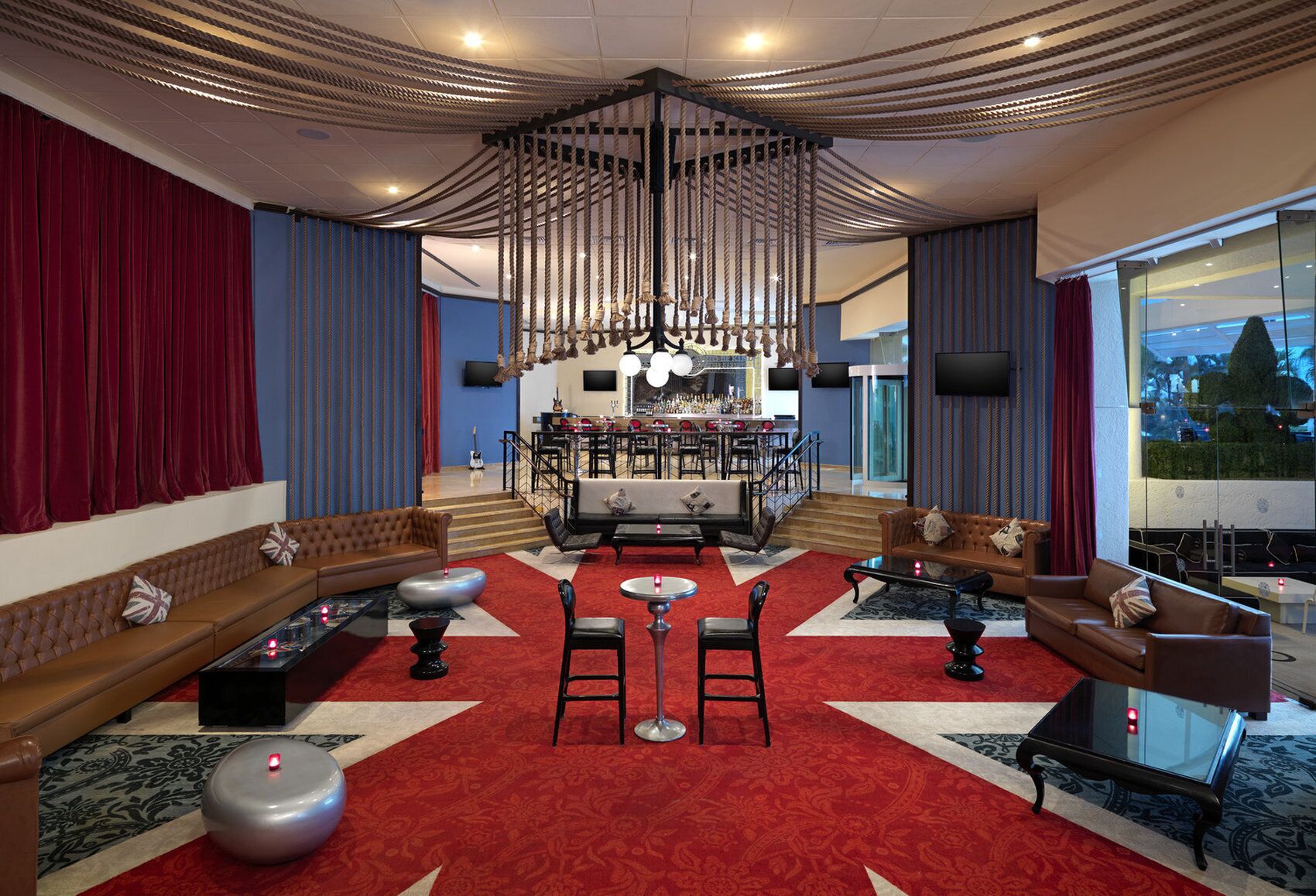 Een ruime hotellobby met een centraal zitgedeelte, een bar en een trap naar een hoger niveau.