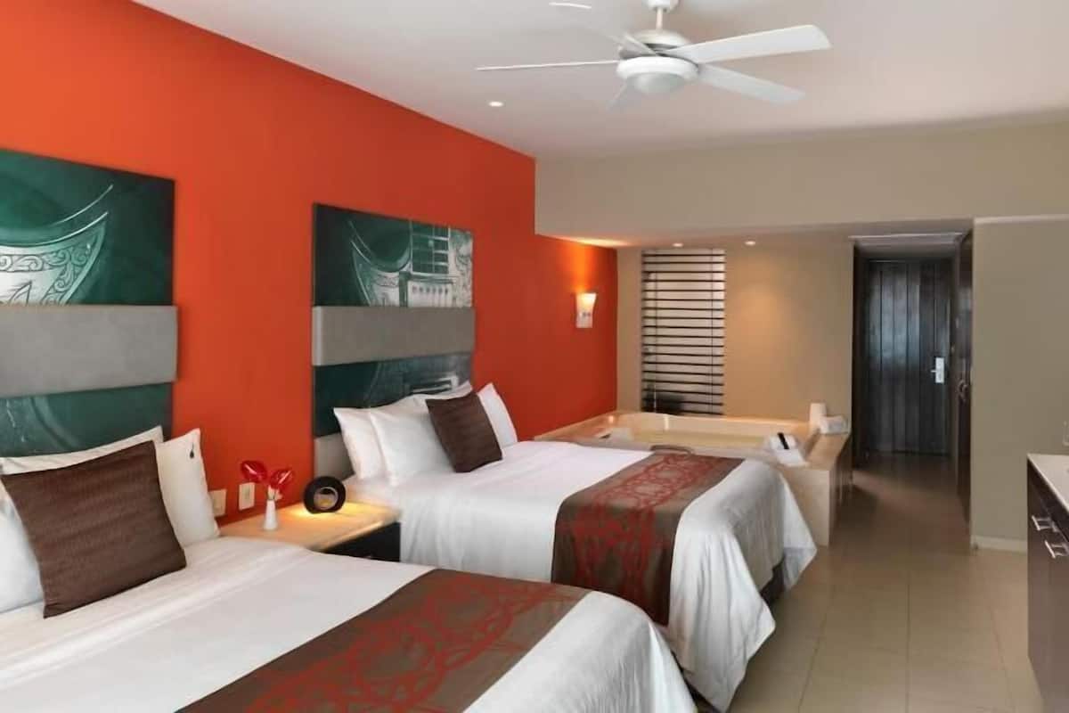 Habitación de hotel con dos camas, televisión, minibar y baño al fondo.
