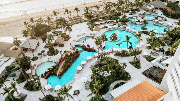 Een resort met meerdere zwembaden, palmbomen en een strand.