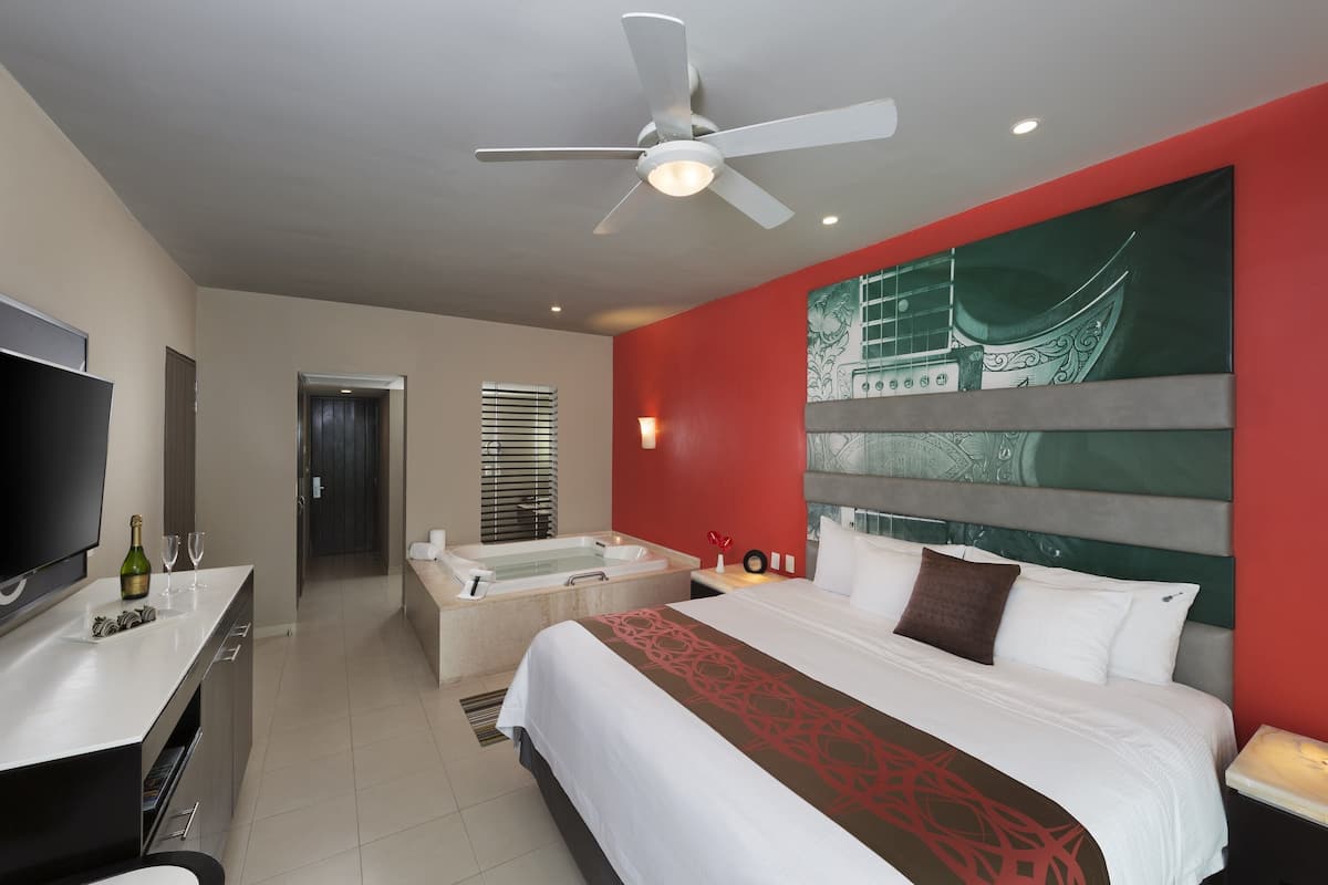 Una habitación de hotel con cama, televisión, escritorio, bañera y ventilador de techo.
