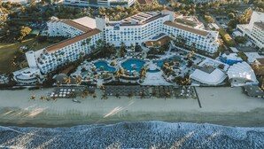 Luchtbeeld van een resort met meerdere gebouwen, een centraal gelegen zwembad en een strand.