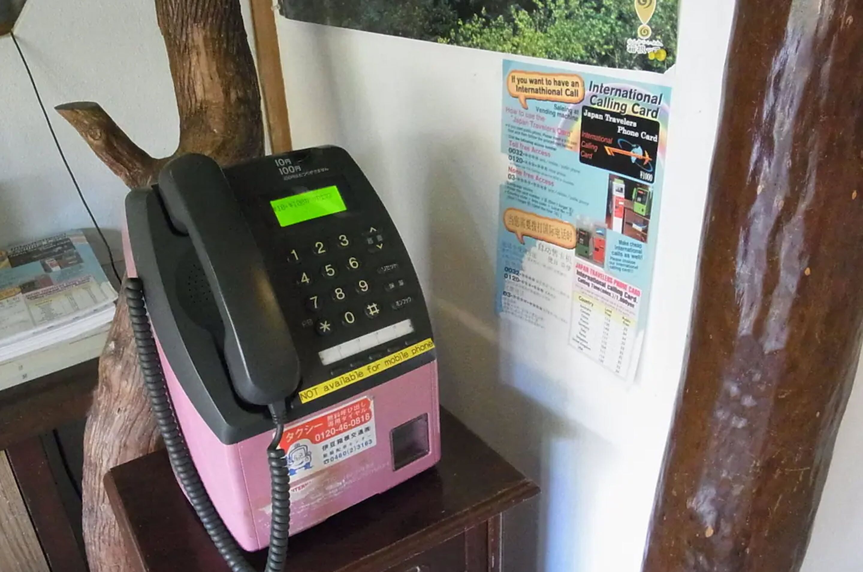 Un teléfono público con base rosa y auricular negro, situado en una habitación con paredes de madera.