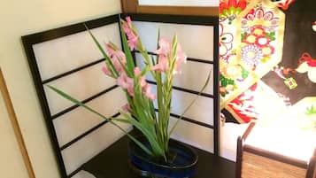 A corner of a room with a black metal chair and a blue vase with pink flowers.
