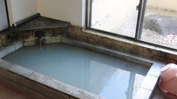 A rectangular indoor pool with clear water, a stone border, and a window with a view of a building outside.