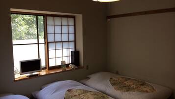 Ein Zimmer mit traditionellem japanischen Shoji-Fenster, einem Nachttisch mit Lampe und einem Bett mit Blumenmuster auf der Bettwäsche.