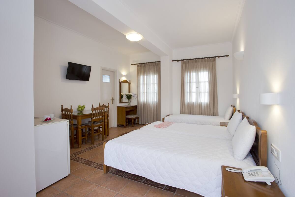 A hotel room with a large bed, a desk with a chair, a television, and a telephone.