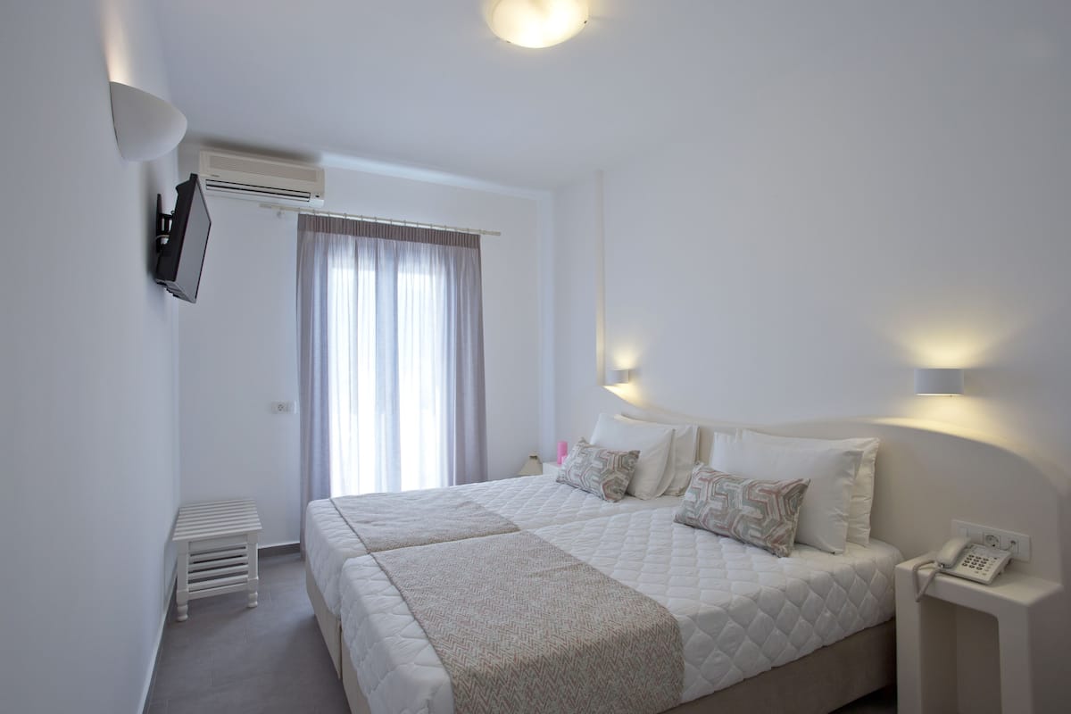 A hotel room with a large bed, bedside tables, a TV mounted on the wall, and an air conditioning unit.