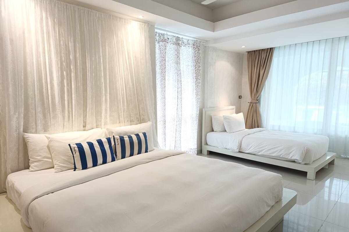 Ein modernes Hotelzimmer mit zwei Betten, einem großen Fenster mit leichtem Vorhang und einem klaren, minimalistischen Design.
