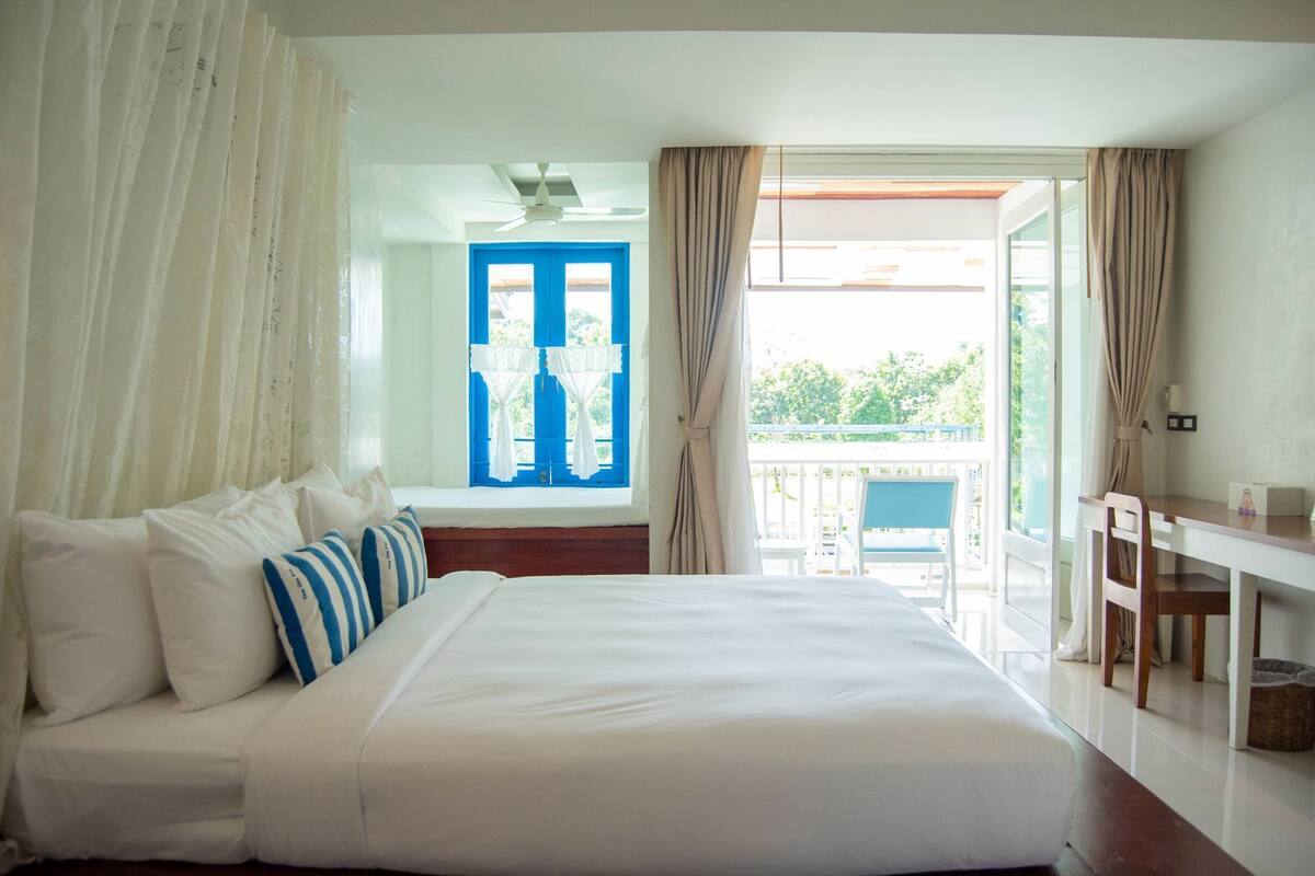 Ein Hotelzimmer mit Bett, Schreibtisch, einem Fenster mit Vorhängen und Blick ins Grüne.