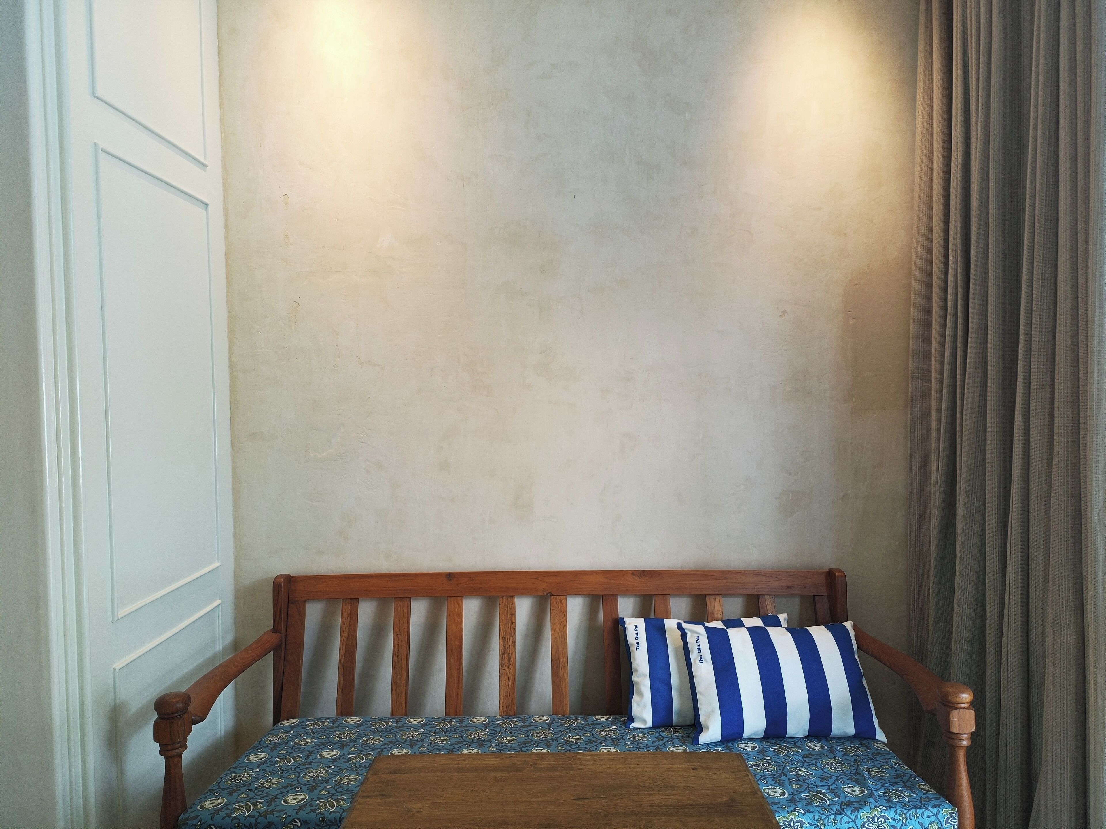 A wooden bench with a patterned cushion and two pillows with blue and white stripes.