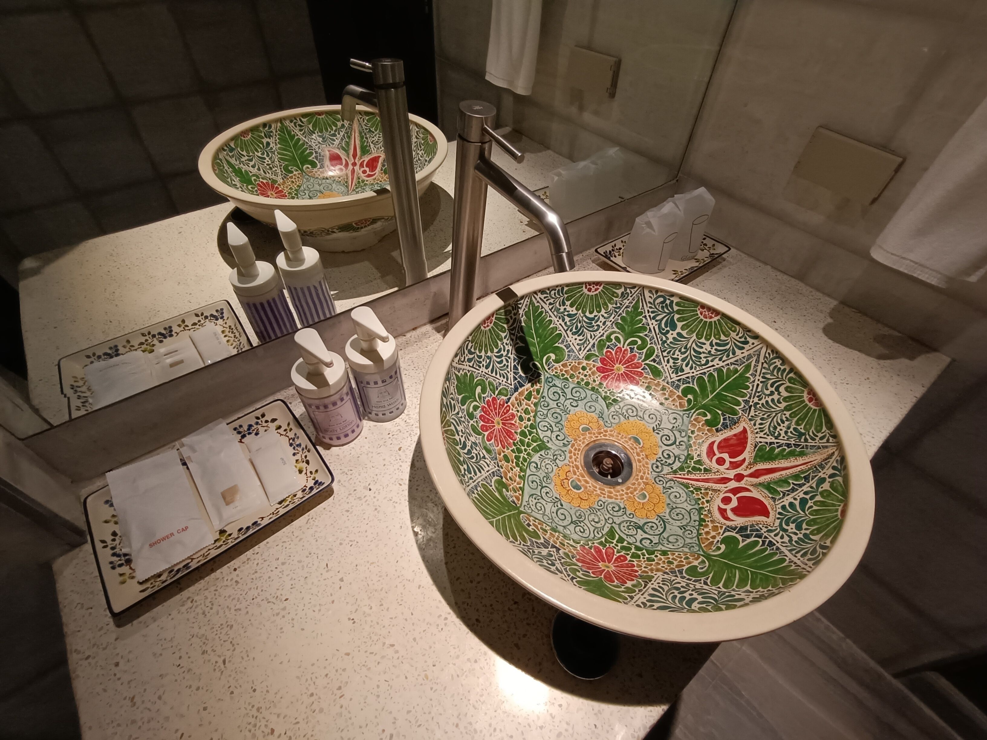 A bathroom with a decorative sink, a mirror, and a tray with toiletries.