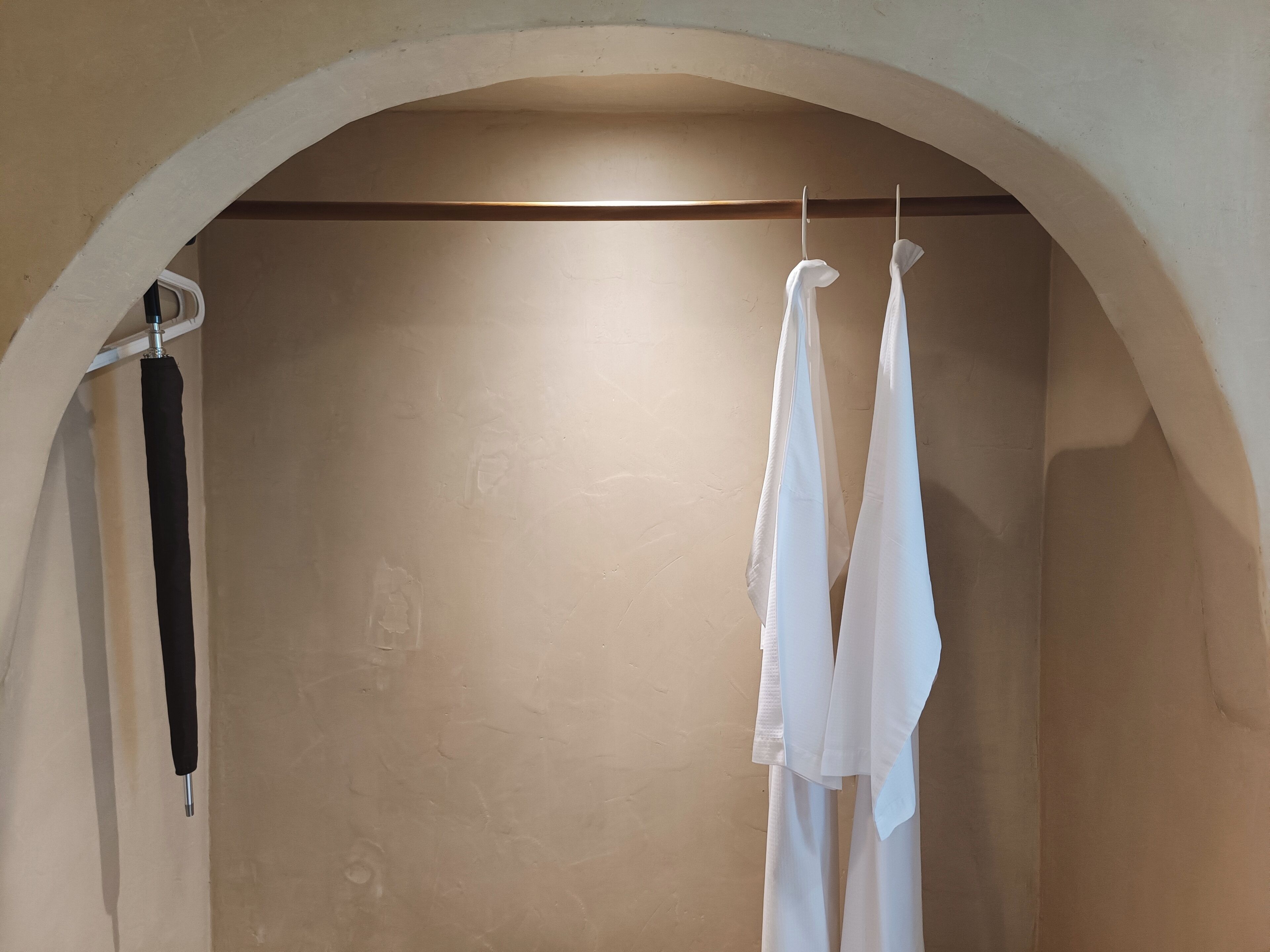 A bathroom with an arched ceiling, a towel rack with two white towels, and a black towel hanging on the left.