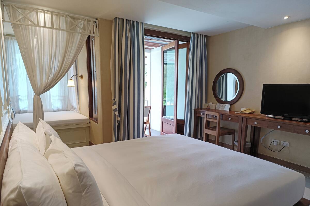 Ein Hotelzimmer mit einem großen Bett, einem Schreibtisch mit Fernseher und einem fenster mit Vorhängen.
