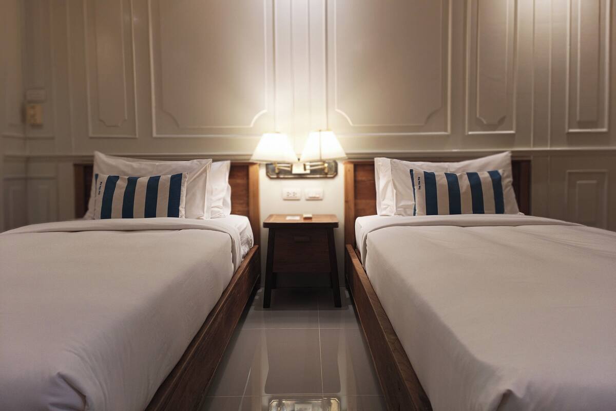 Ein Hotelzimmer mit zwei Betten, einem Nachttisch und einer Lampe dazwischen.