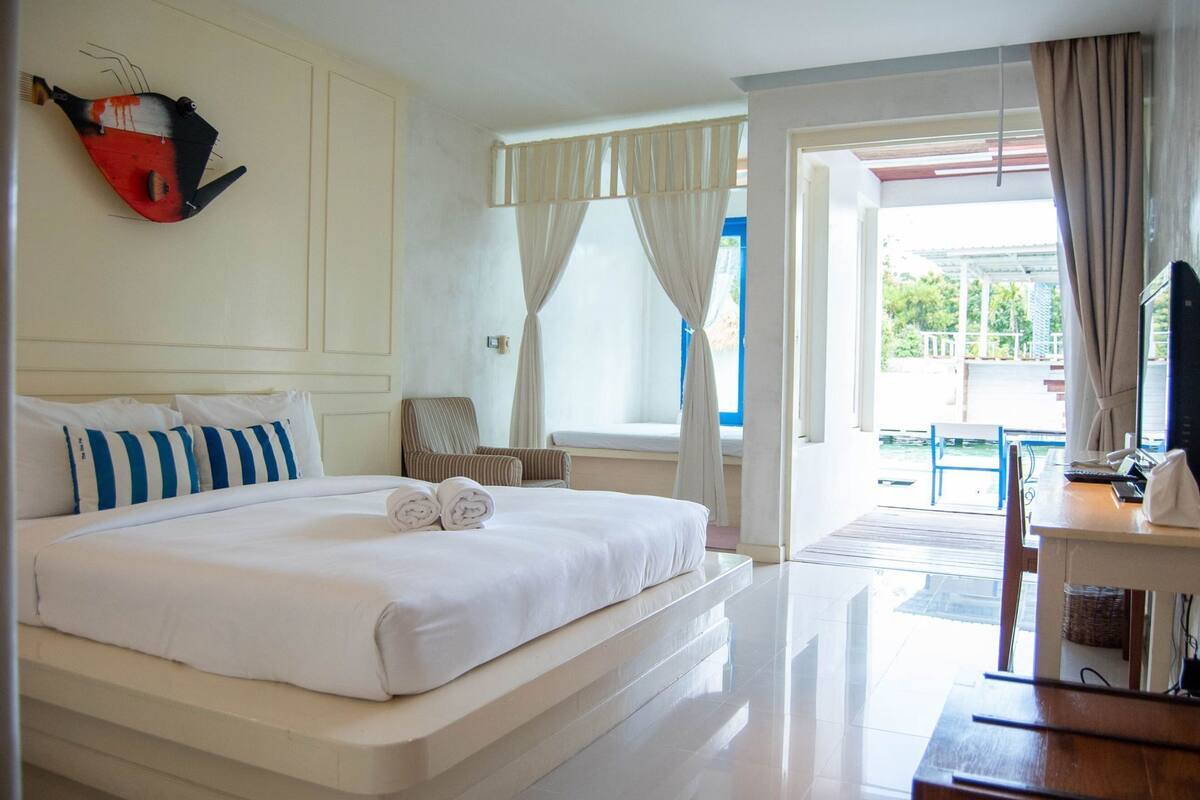 Ein Hotelzimmer mit Bett, Stuhl, Schreibtisch mit Computer und Blick ins Freie.