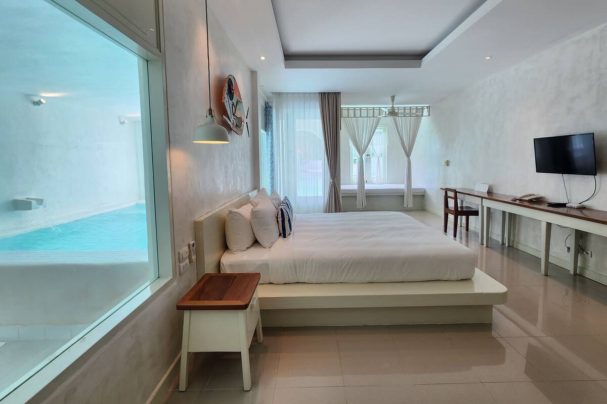Ein modernes Hotelzimmer mit einem großen Bett, einem Schreibtisch mit Fernseher und Blick auf einen Pool.