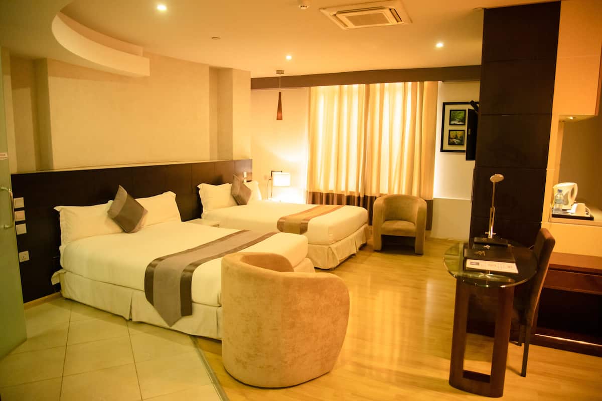 A hotel room with a large bed, a separate sofa bed, a small armchair, a glass table, and a desk with a chair.