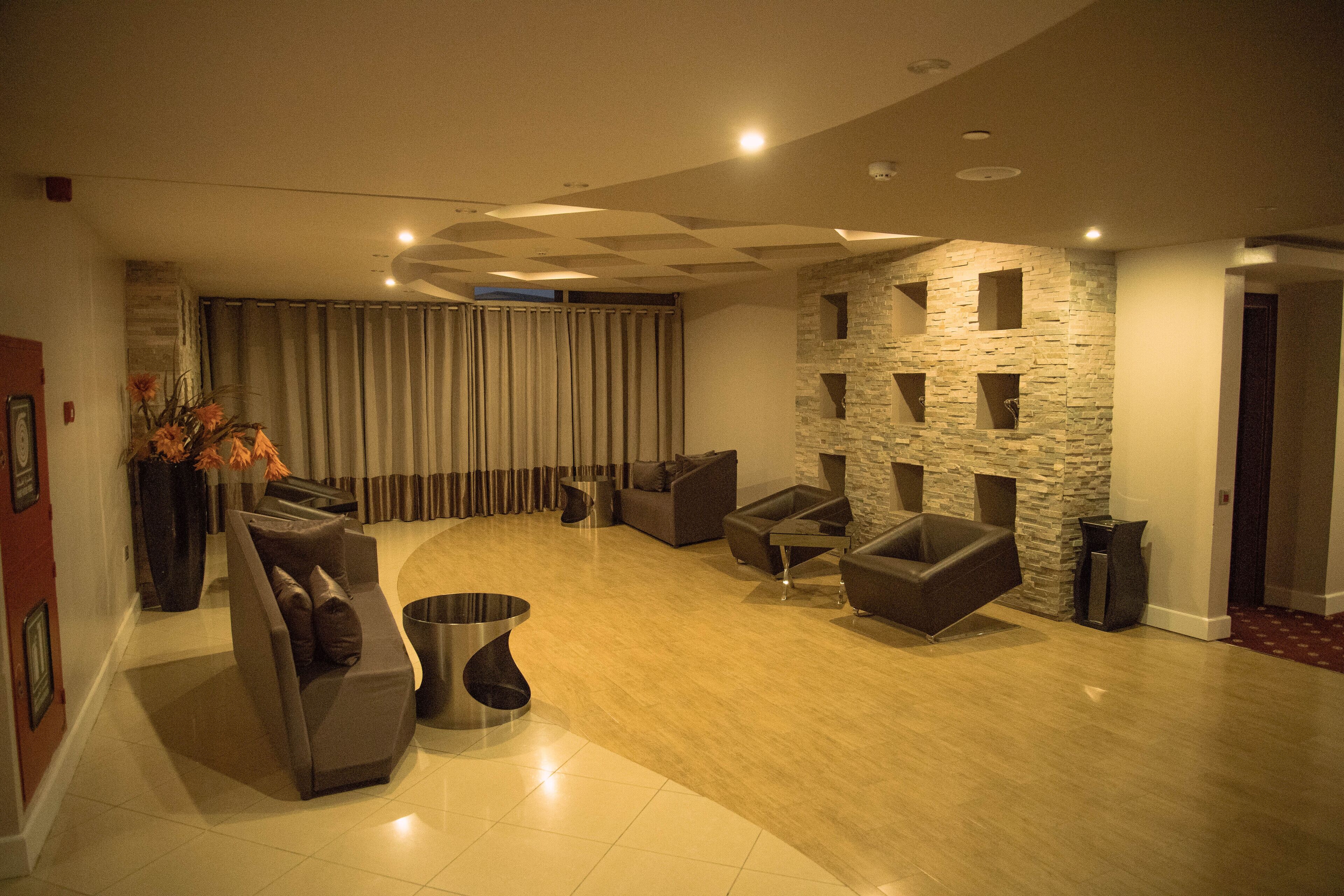 A modern living room with a curved sofa, armchairs, and a coffee table. There is a stone accent wall and a large window with curtains.