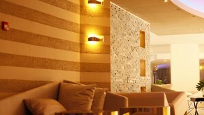 A modern lobby with a striped wall, a textured wall with cutouts, and a seating area with a sofa and armchairs. - SG Premium Resort (Arusha)