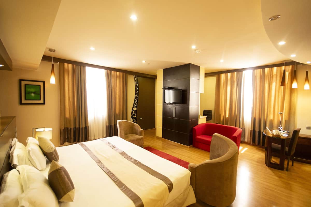 A hotel room with a large bed, a red sofa, a TV, and a dining area.