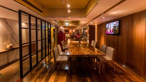 A modern restaurant interior with a wooden dining table, cushioned chairs, a television mounted on the wall, and a marble accent wall. - Inhouse Hotel (Taipei)