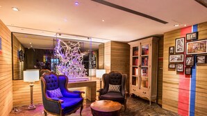 Una habitación con paredes de madera, un espejo grande, un sillón azul, un sillón oscuro, un armario de madera con puertas de vidrio y un piso de mármol.