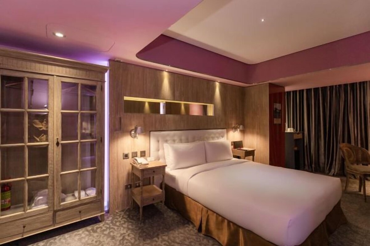 Una habitación de hotel con una cama grande, un armario, una mesita de noche y una silla.