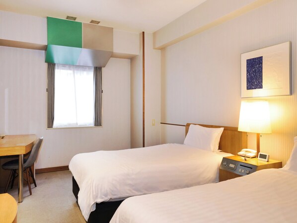 Habitación de hotel con dos camas, un escritorio, una silla, una lámpara y un cuadro en la pared.